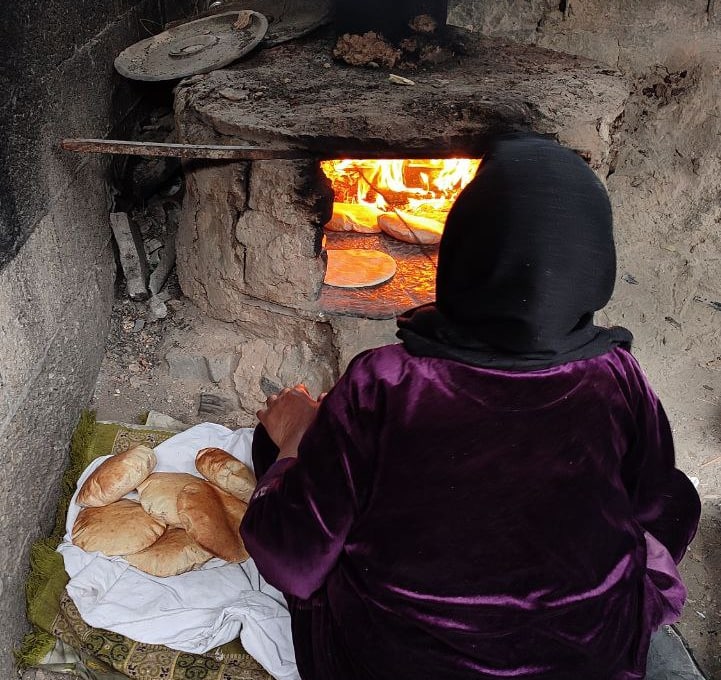 A person tends bread in a wood-fired oven in Gaza, with baked flatbreads beside them.