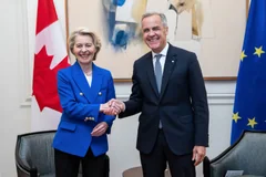 Mark Carney and Ursula von der Leyen shaking hands between Canadian and European Union flags.