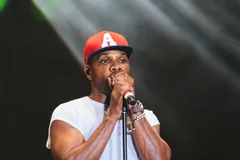 Kirk Franklin performing with a microphone and red cap at JoyFest ’17 in an archive photograph.