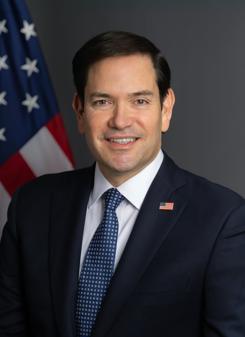 Marco Rubio in his official January 2025 portrait, wearing a dark suit and blue tie beside a U.S. flag.
